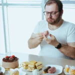 Man eating sweets and pastries, highlighting dietary factors associated with Jacksonville Men’s Clinic obesity care.