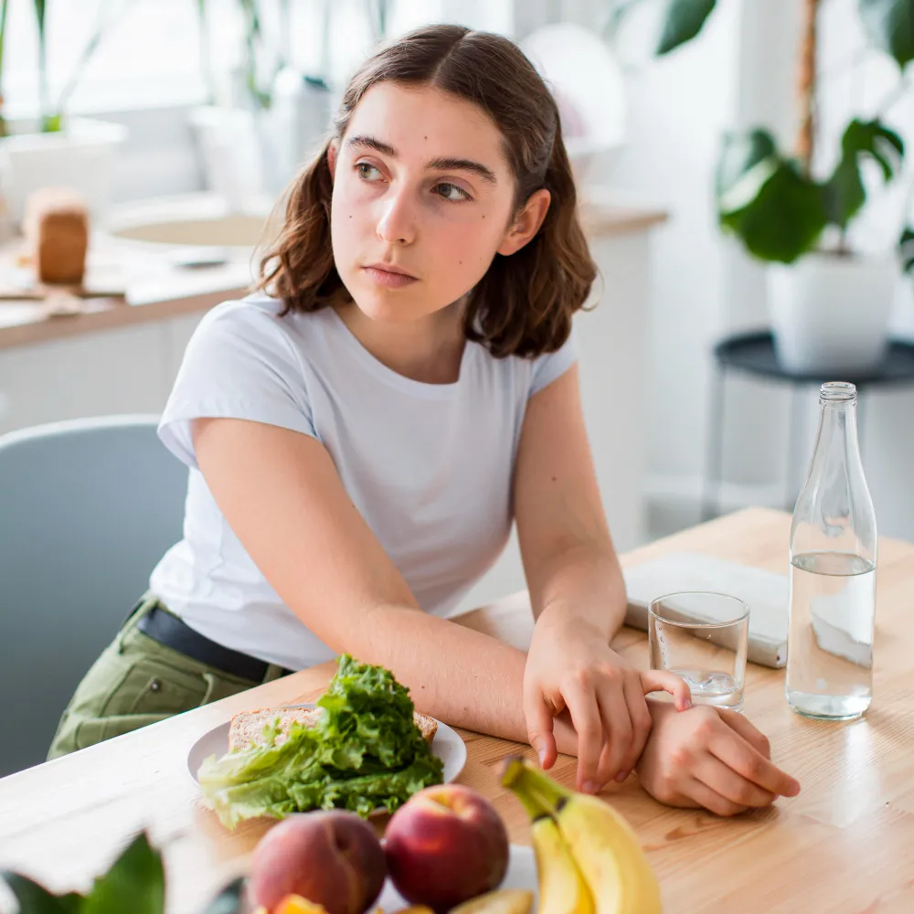 Teen girl sitting thoughtfully with healthy food, highlighting emotional struggles related to eating disorders Jacksonville and the importance of seeking specialized care and excessive anger treatment Jacksonville