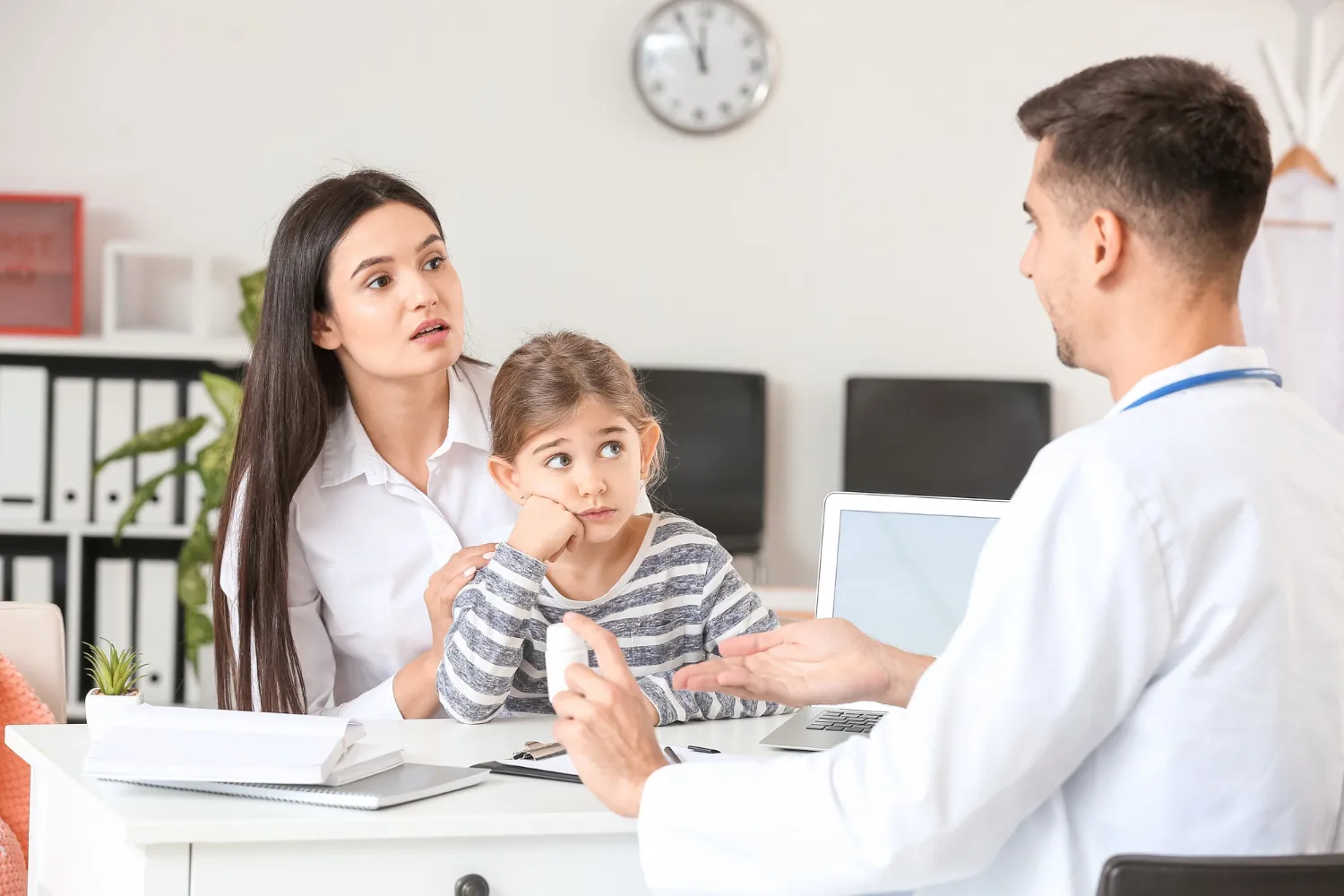 Family primary care physician discussing child’s health concerns with mother at local health care clinic