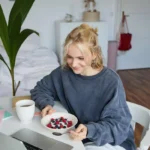 Young woman eating a healthy meal while working from home, representing awareness around overall wellness and preventive care, including regular STD testing and health checkups