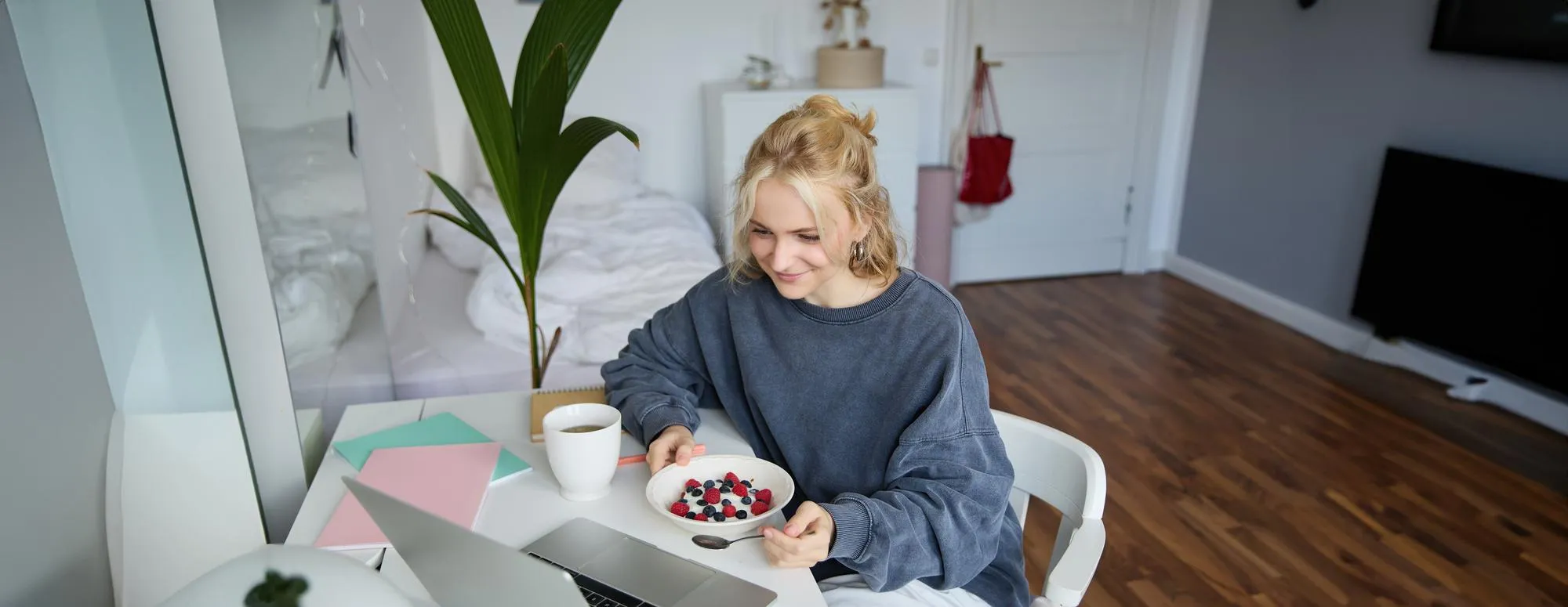 Young woman eating a healthy meal while working from home, representing awareness around overall wellness and preventive care, including regular STD testing and health checkups