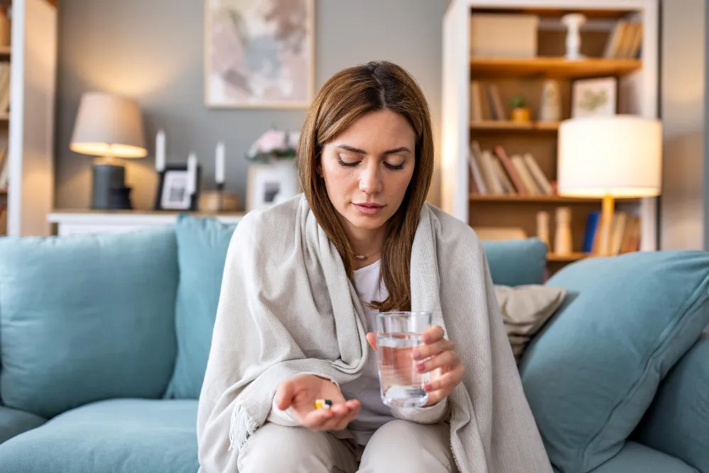 Woman taking pills with water at home highlighting womens primary care services and women's health in Jacksonville
