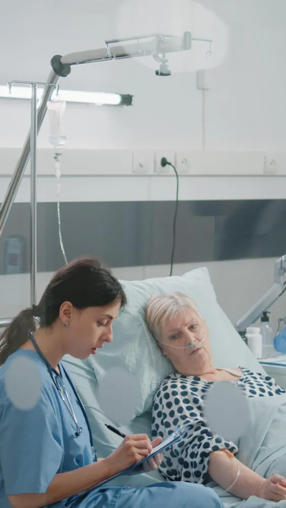 Nurse monitoring elderly patient in hospital room as part of geriatric healthcare and senior medical care services