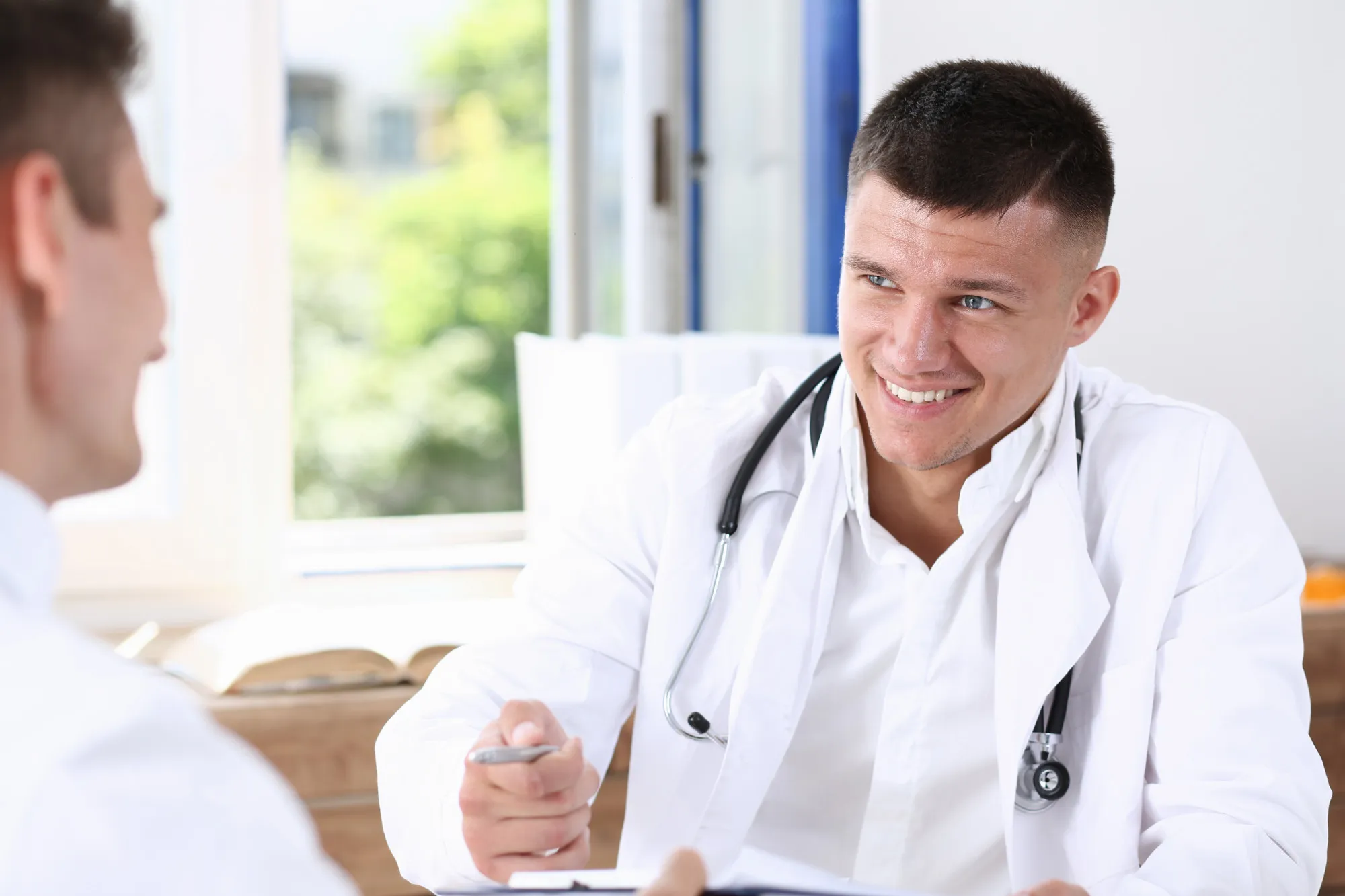 A male doctor discussing health concerns with a patient during a consultation, representing professional guidance from a Men's Health Specialist and support for men's wellness.